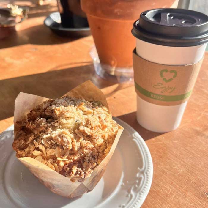 An oat-topped muffin from the Pivot Brew menu on a plate next to a paper coffee cup.
